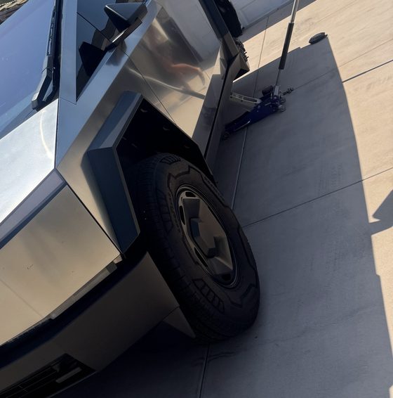 Rear wheel of a Cybertruck with the jack set up beside it on a residential driveway