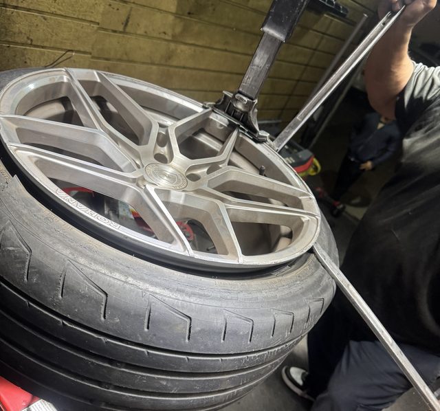 Low-profile performance tire being levered onto a silver split-spoke alloy wheel with a tire bar